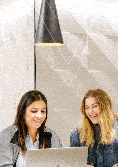 Two people are looking at the laptop and smiling while sitting in a corner