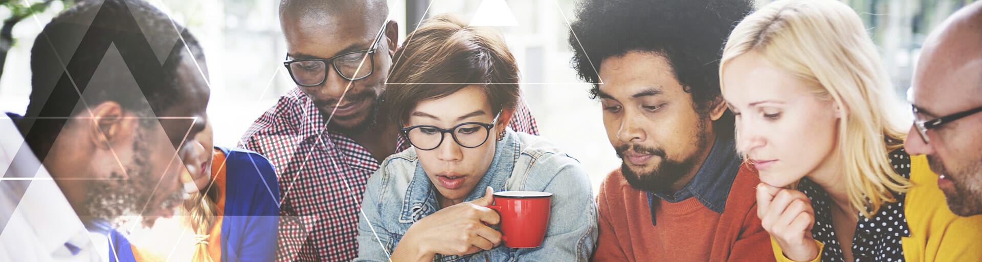 A group of people focusing on something on the table and one person is holding a cup